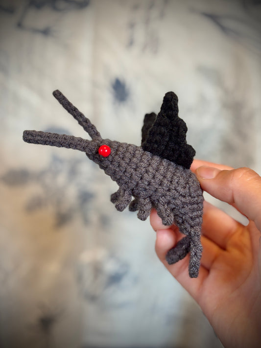 Hand holding a small grey shrimp with black bat wings