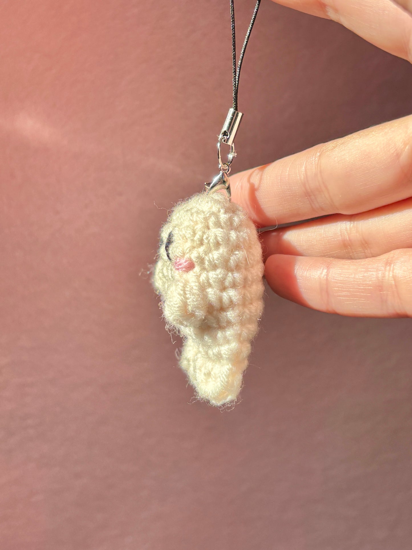 Hand holding a small crocheted heart charm against a plain background