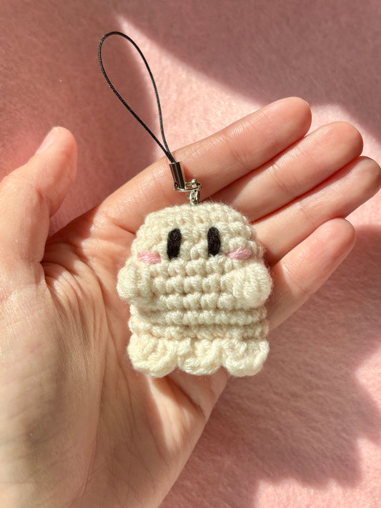 Small crochet ghost charm held in a hand against a pink background