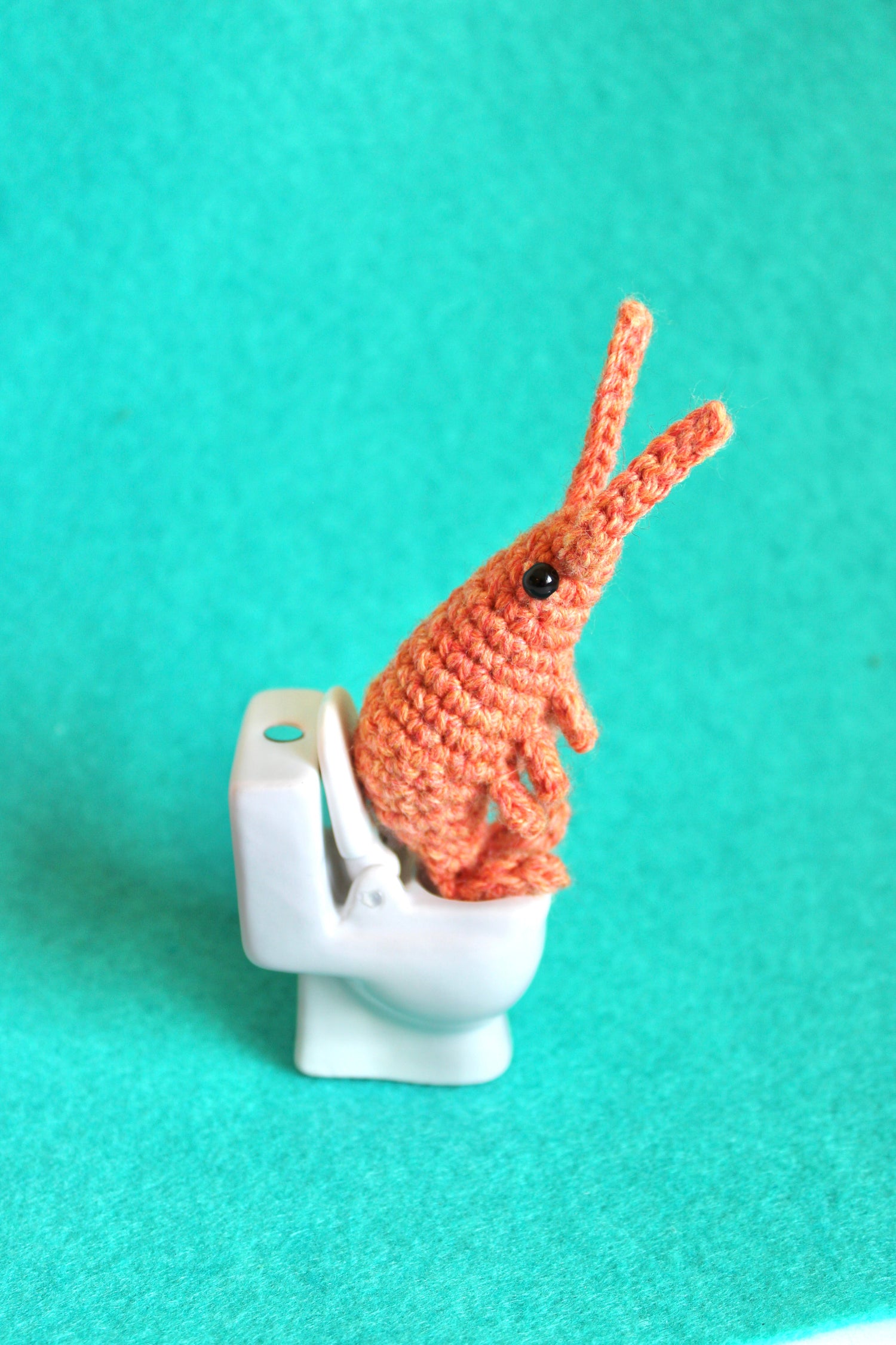 A small crocheted shrimp sitting on a miniature porcelain toilet