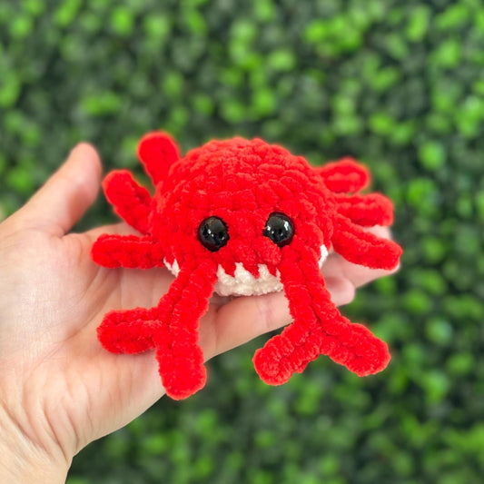 Hand holding a soft red crochet crab toy against a green textured background