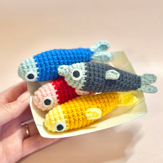 Colorful crochet fish toys on a white tray held by a hand against a beige background