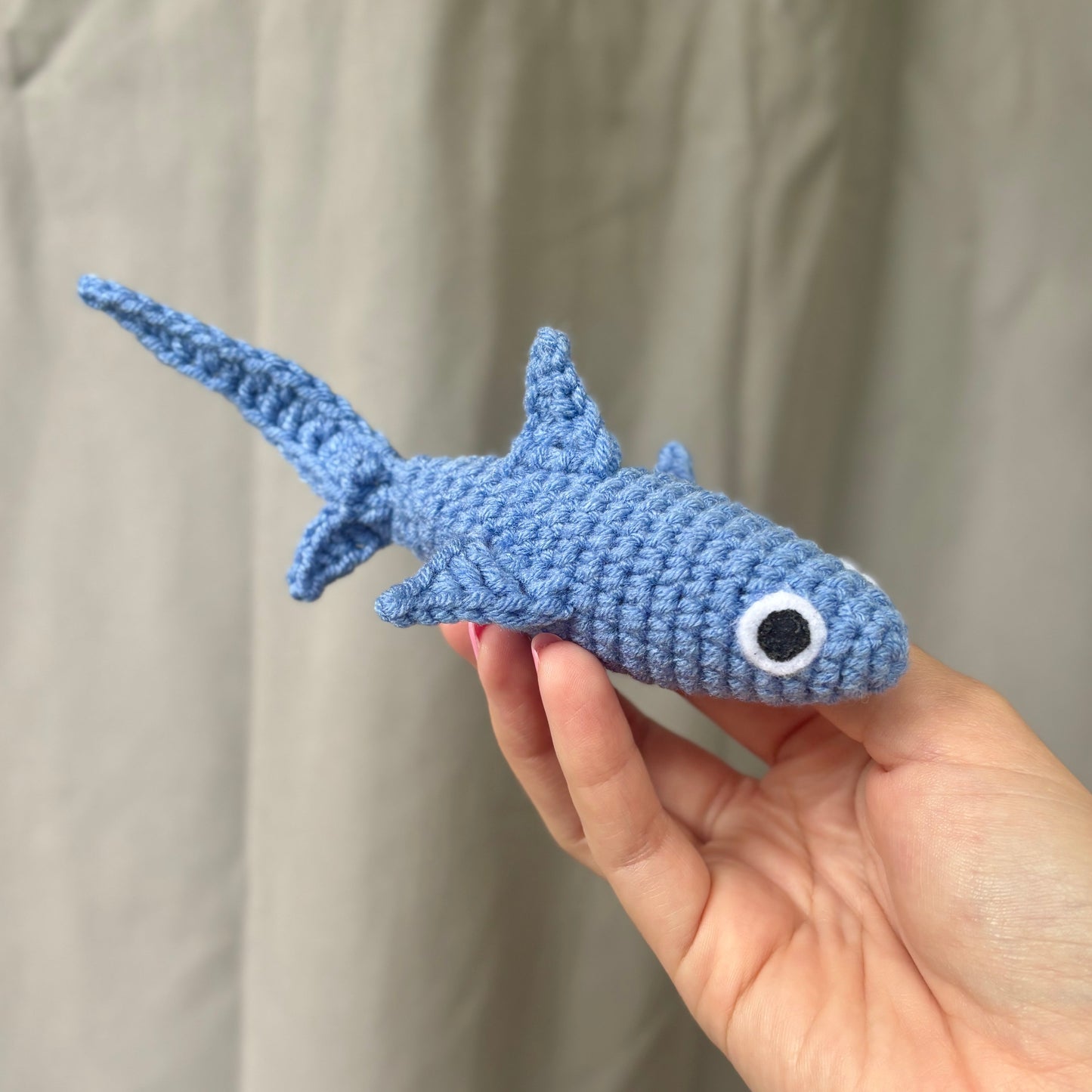 Hand holding a blue crocheted shark toy against a plain background