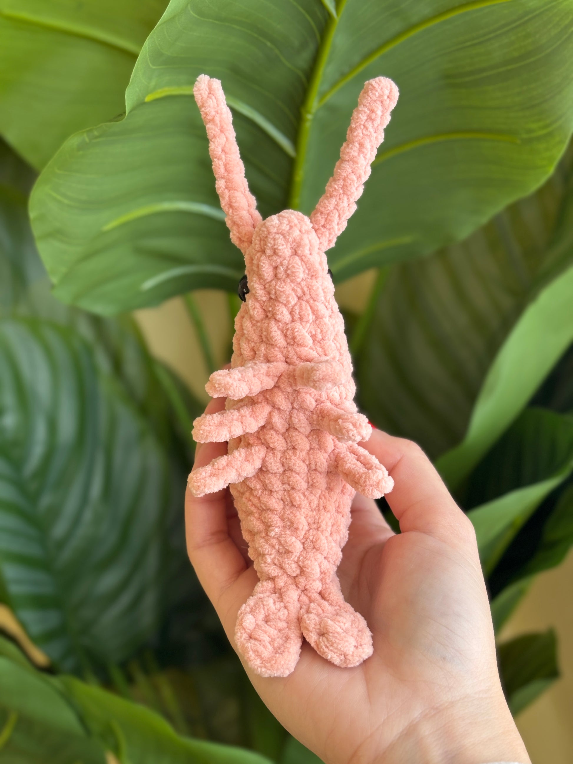 Pink crochet plushie held in front of green leaves