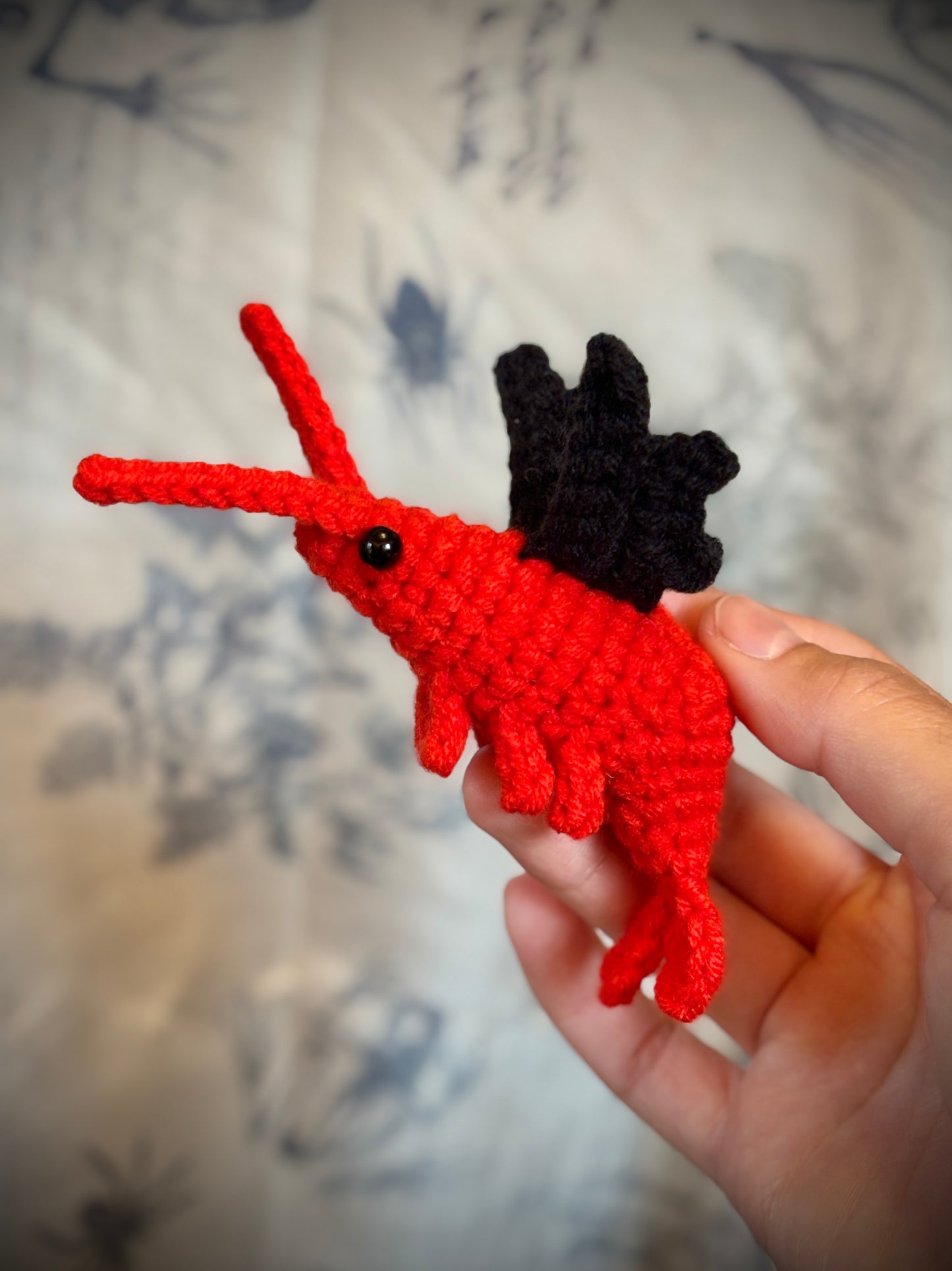 hand holding a red shrimp with black bat wings

