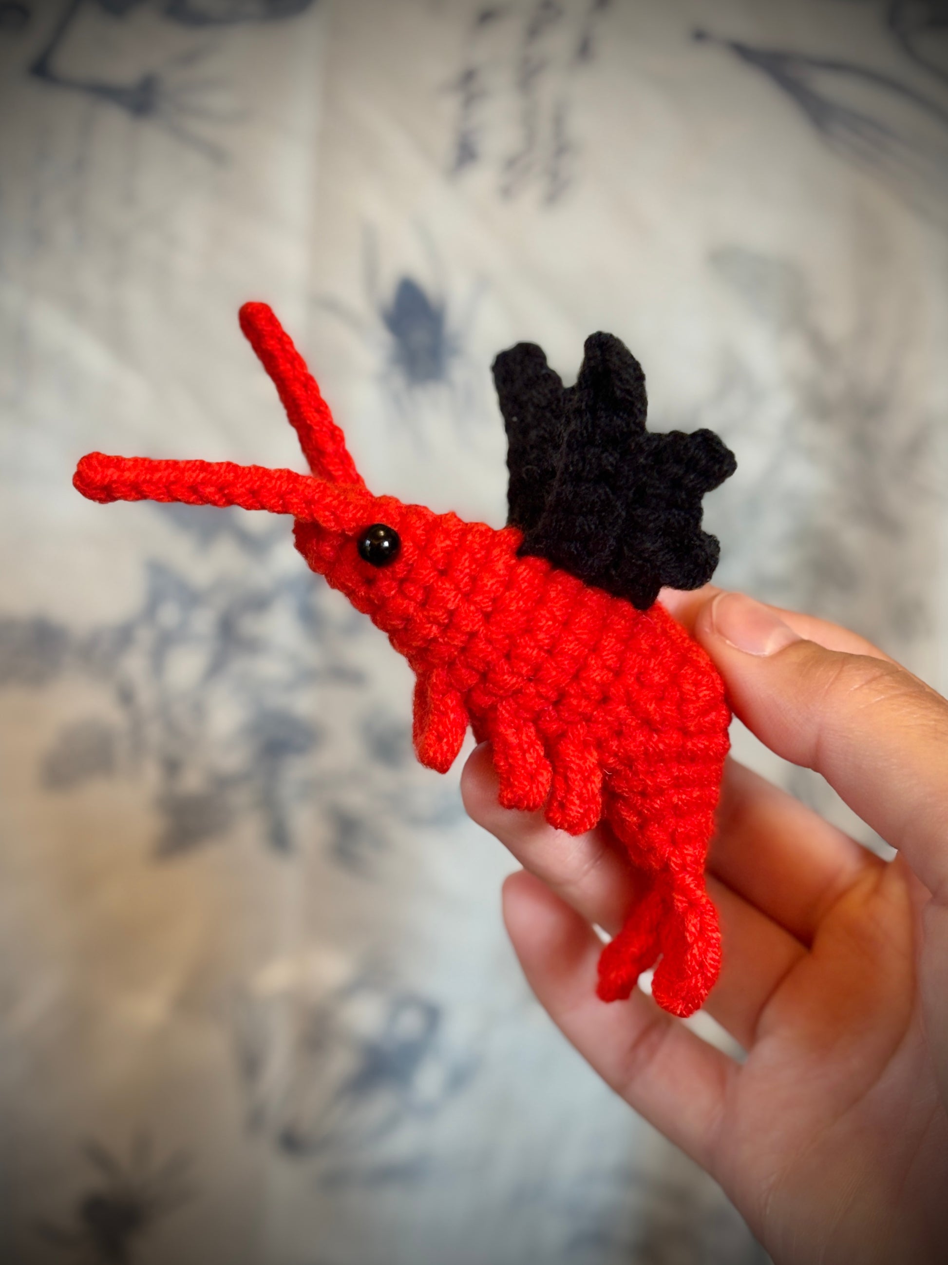 hand holding a red shrimp with black bat wings
