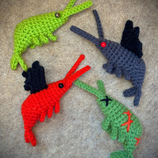 Four colorful crocheted shrimp plushies on a textured surface