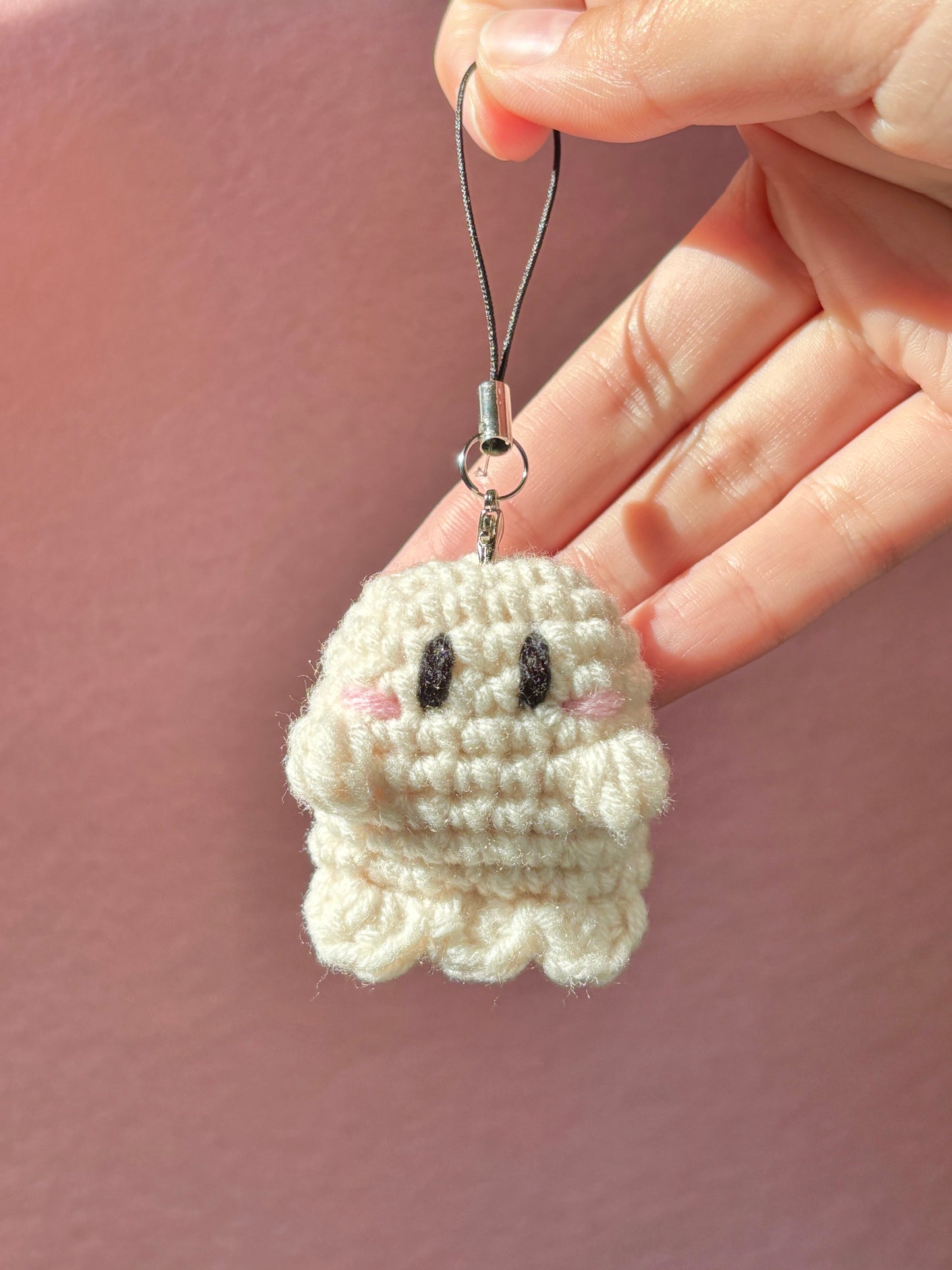 Small crocheted ghost charm held by a hand against a pink background