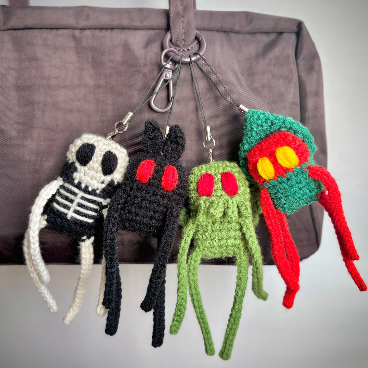 Four colorful crochet monster keychains hanging from a bag.
