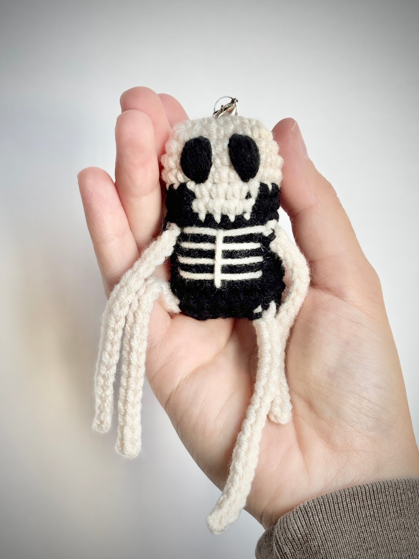 Hand holding a small crochet skeleton keychain against a plain background