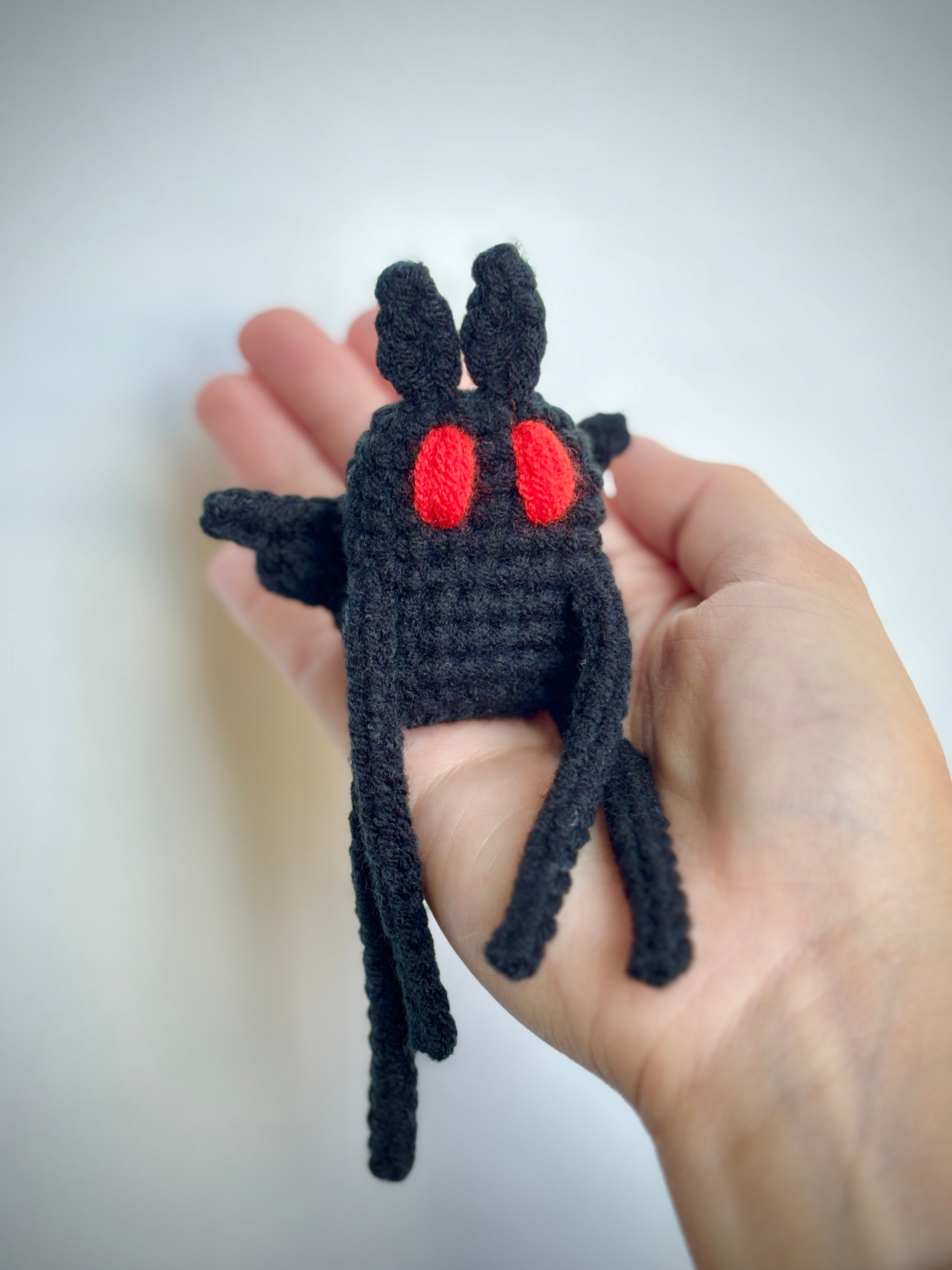 Hand holding a small mothman plush against a plain background