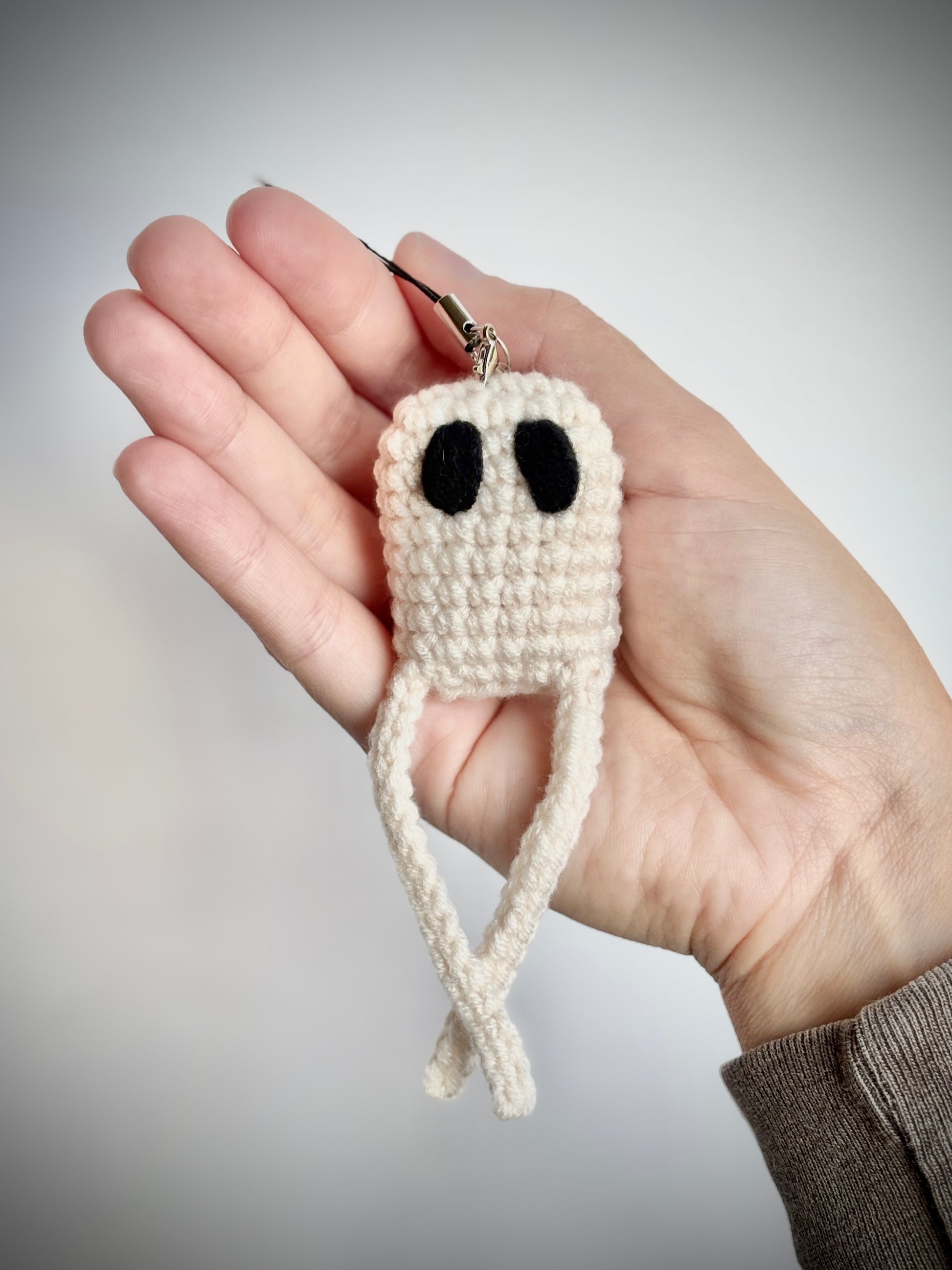 Hand holding a small crochet nightcrawler keychain against a neutral background