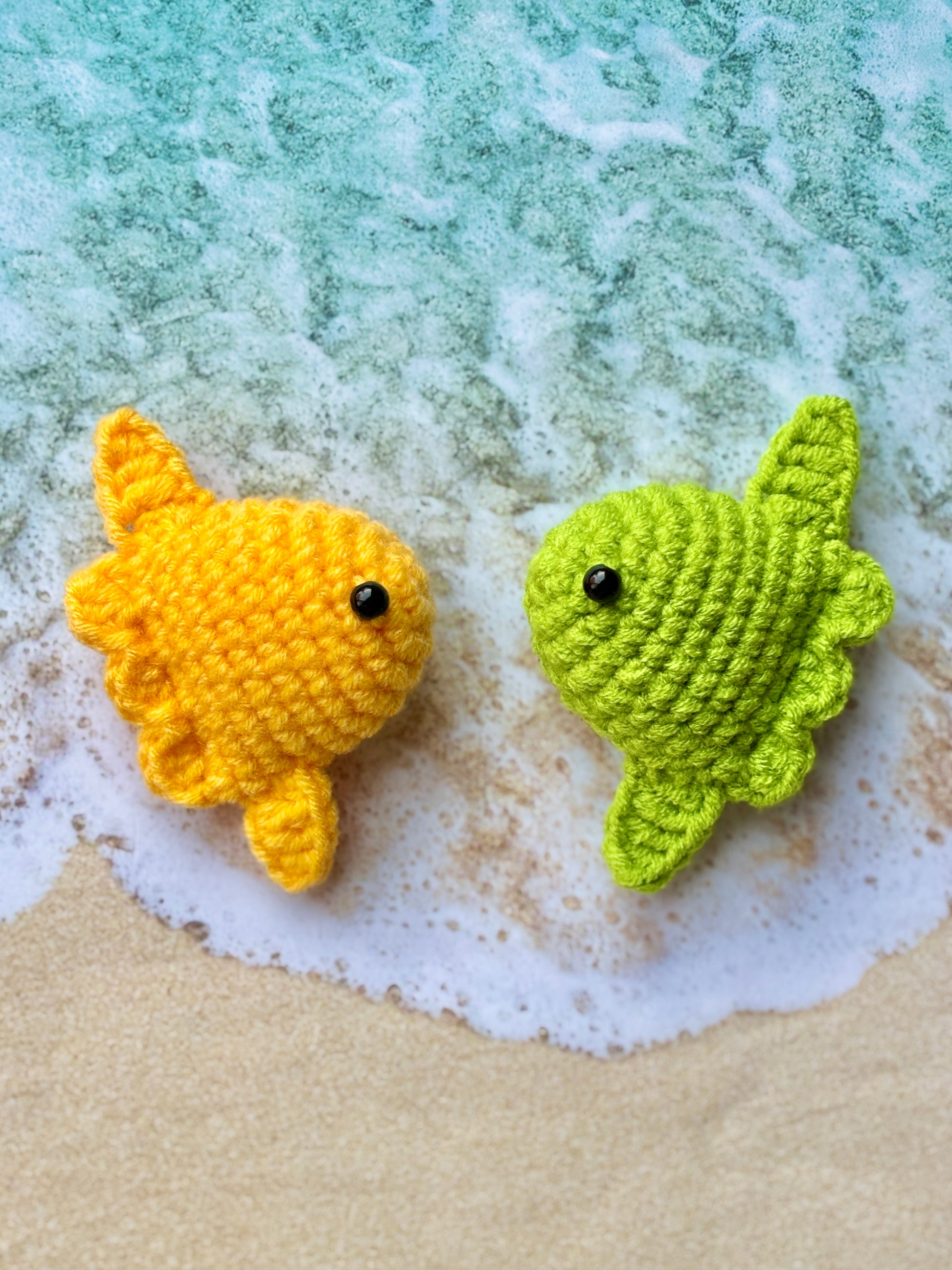 Two crocheted fish, one yellow and one green, on a textured surface.