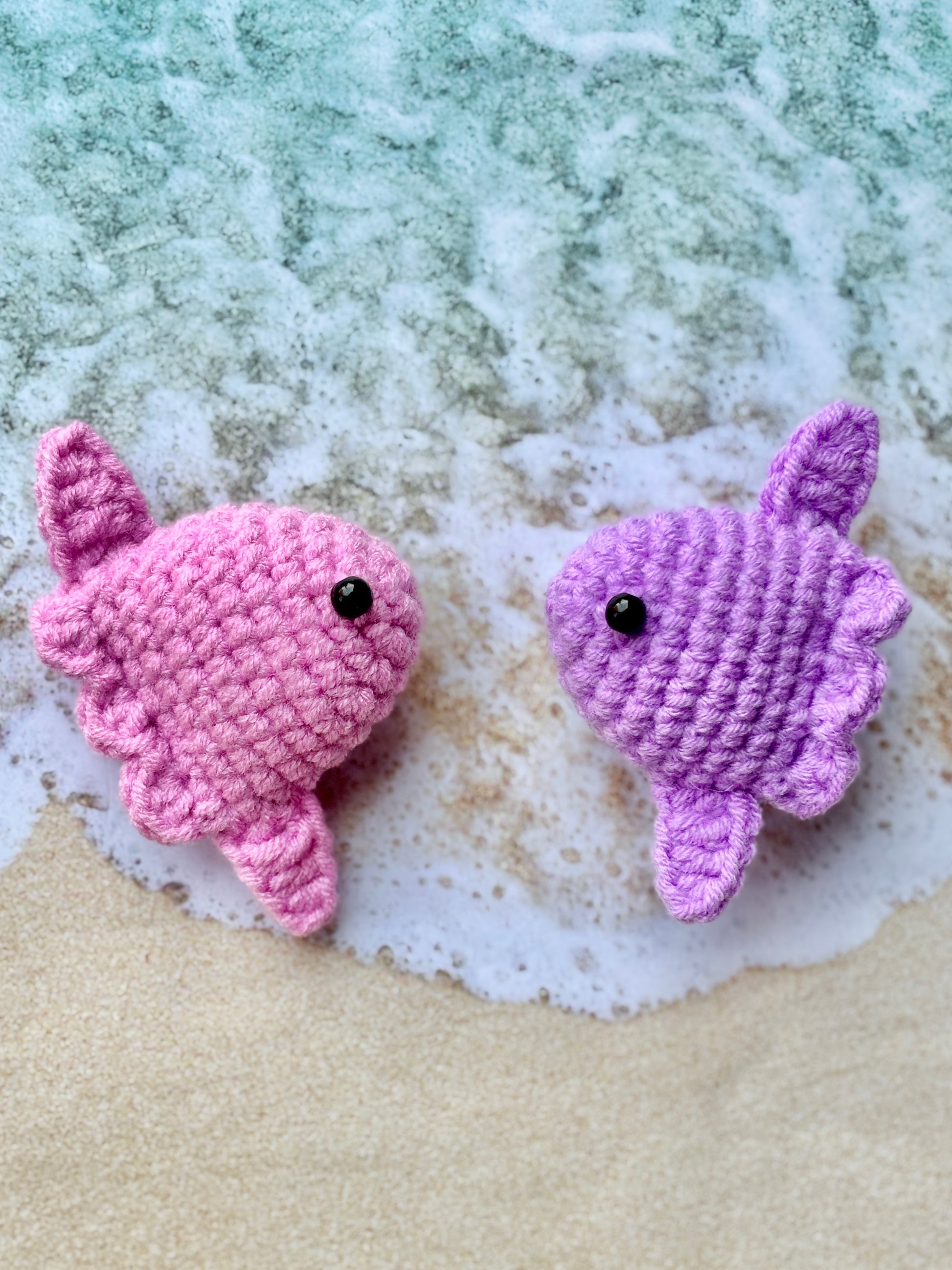 Two crocheted sunfish, one pink and one purple, on a textured surface.