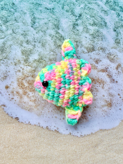 Colorful crocheted fish  on a beach with waves.