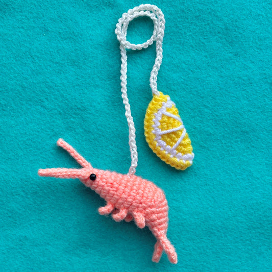 Crocheted pink shrimp and yellow lemon on a turquoise background